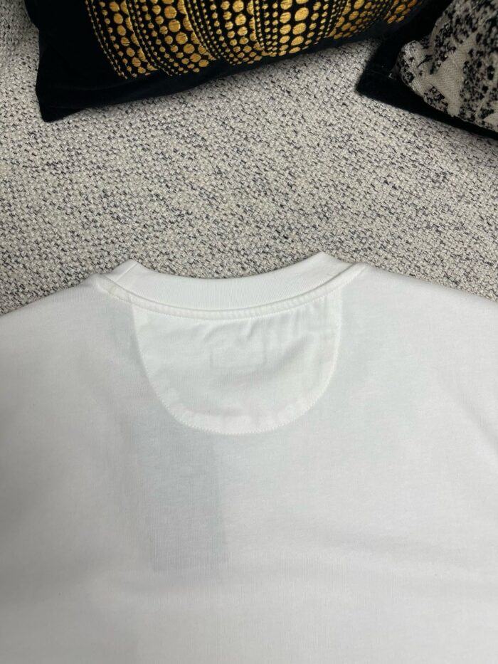 Maglietta bianca semplice su sfondo tessuto, ambiente accogliente e di stile casual elegante.