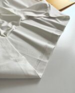 Tessuto bianco in cotone, elegante e versatile, con dettagli di cucitura e drappeggio morbido.
