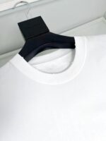 Maglietta bianca con scollo classico e gancio nero elegante, dettaglio vicino alla cucitura.