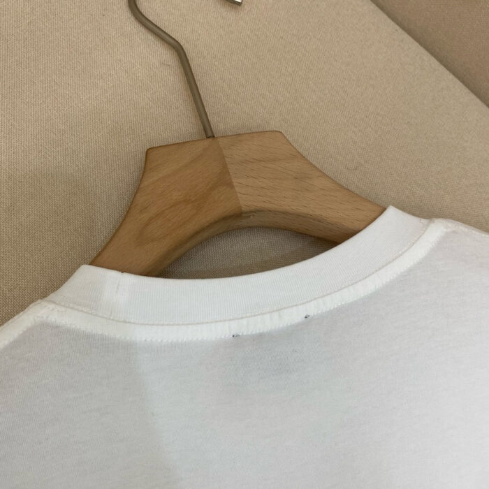 Maglietta bianca a girocollo su gancio di legno, stile casual e minimalista.