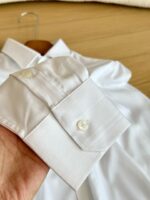 Camicia bianca elegante con polsino raffinato, tessuto liscio e rifinito su sfondo di legno caldo.
