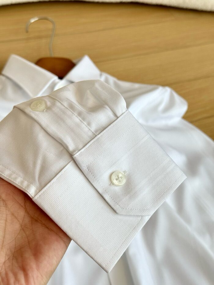 Camicia bianca elegante con polsino raffinato, tessuto liscio e rifinito su sfondo di legno caldo.
