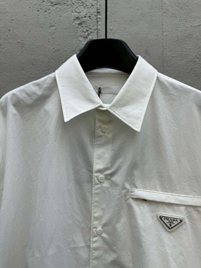 Camicia bianca elegante con logo triangolare, stile raffinato e moderno per occasioni formali.