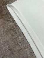 Tessuto bianco rifinito su sfondo velluto elegante, dettaglio di cuciture e texture morbida.