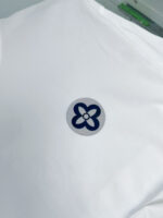 Maglietta bianca con logo floreale blu, stile minimalista e elegante, ideale per look casual e raffinati.