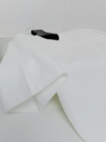 Camicia bianca elegante su sfondo neutro, appesa a gancio nero, minimalismo e stile raffinato.