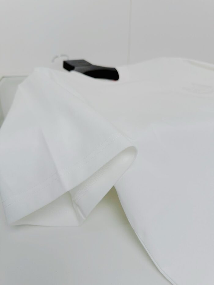 Camicia bianca elegante su sfondo neutro, appesa a gancio nero, minimalismo e stile raffinato.