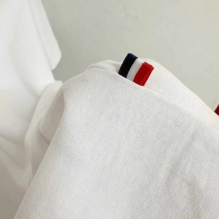 Maglietta bianca con dettagli a strisce rosso, bianco e blu, stile casual e sportivo.