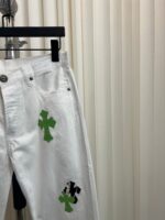 Jeans bianchi con croci verdi e patch decorativi, stile streetwear moderno e di tendenza.