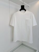 Maglietta bianca semplice con tasca decorativa, ideale per outfit casual e stile minimalista.