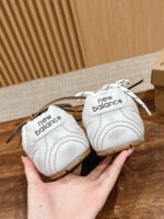 Sneakers New Balance bianche frontali, con dettagli neri, su superficie in legno, stile casual.