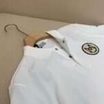 Maglietta polo bianca con ricamo circolare, stile elegante e versatile su appendiabiti semplice.