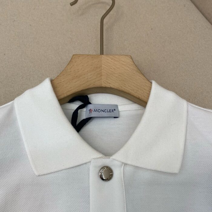 Polo Moncler bianca elegante con colletto strutturato e bottone metallico lucido.