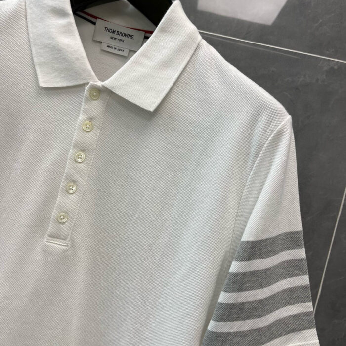 Maglietta polo bianca con dettagli a righe grigie, stile classico e design moderno elegante.