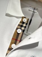 Camicia polo bianca elegante con dettaglio check ispirato a Burberry e bottoni raffinati.