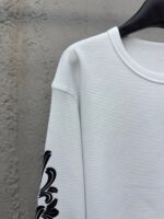 Maglietta bianca con dettaglio floreale nero sulla manica e colletto a girocollo, stile casual elegante.