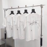 Magliette bianche con stampa moderna e astratta, stile urban su doppia fila su supporto metallico.