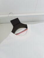 Maglietta bianca casual con colletto a strisce e appendino nero, stile minimalista e moderno.
