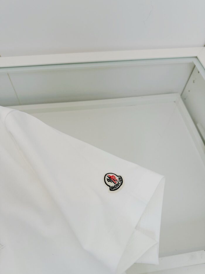 Camicia bianca elegante con logo ricamato, esposta in vetrina minimalista e luminosa.