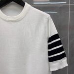 Maglietta bianca con dettagli a righe nere sulle maniche, stile casual e sporty.