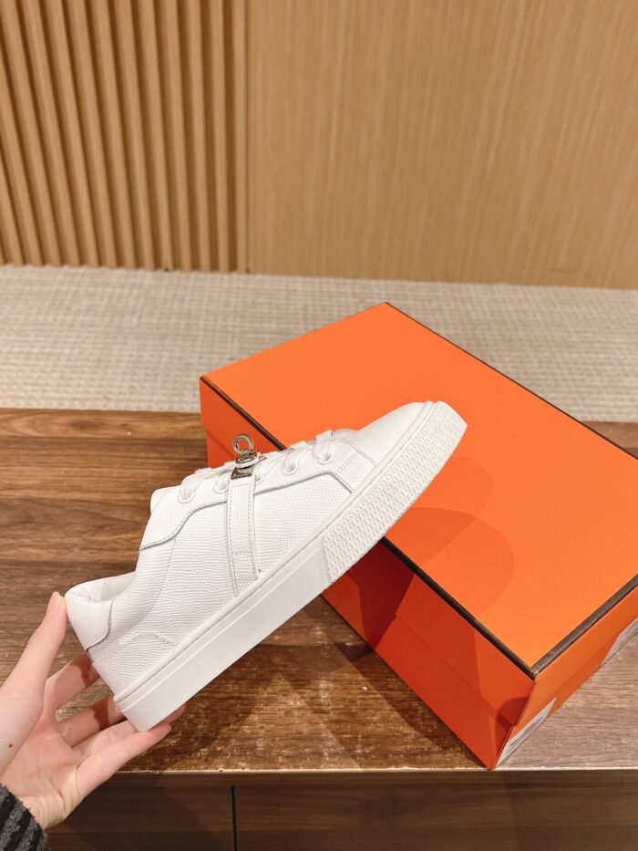 Sneaker bianco minimalista con scatola arancione e sfondo in legno, stile moderno e di qualità.