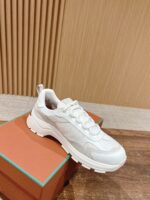 Scarpa sneakers bianca moderna su scatola arancione e turchese, con suola robusta e design elegante.