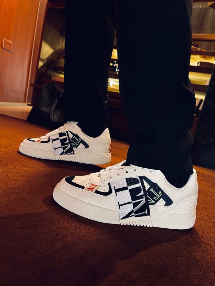 Sneakers bianche con grafiche creative e dettagli moderni, abbinati a pantaloni scuri eleganti.