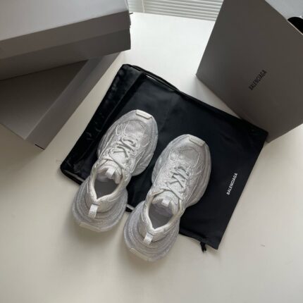 Sneaker bianche minimaliste, scatole grigie e tasca nera su superfice riflettente elegante.
