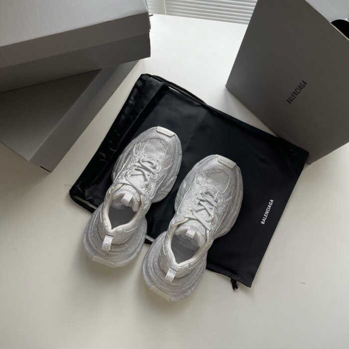 Sneaker bianche minimaliste, scatole grigie e tasca nera su superfice riflettente elegante.