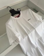 Maglietta bianca minimalista con logo sul petto e colletto rosso, stile moderno e versatile.
