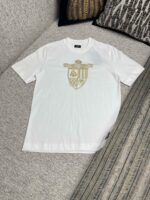Maglietta bianca con logo a scudo dorato, stile casual ed elegante.