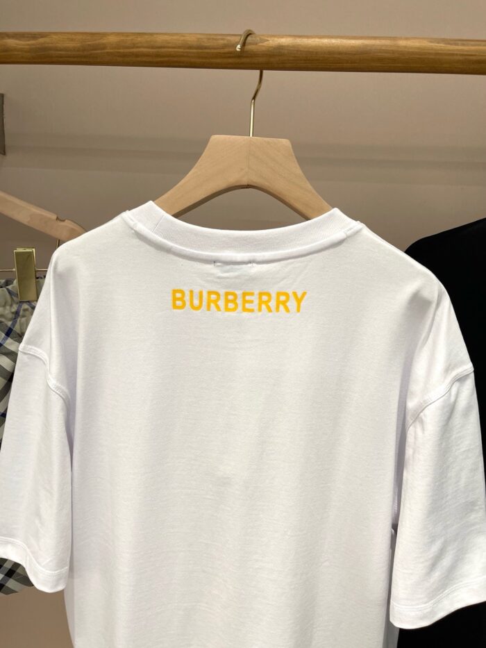 T-shirt bianca Burberry con logo giallo ricamato sul retro, cotone morbido, stile classico.