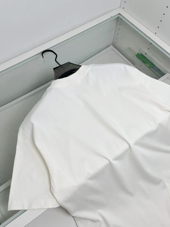 Maglietta bianca semplice appesa su sfondo neutro, stile minimalista ed elegante.