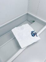 T-shirt bianca con logo serpente blu in esposizione elegante su vetrina moderna simmetrica.