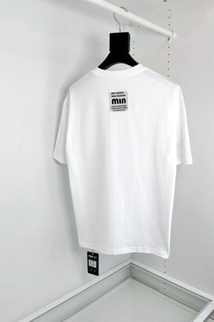 T-shirt bianca minimalista con etichetta MIA, vestibilità elegante, ideale per uno stile moderno e versatile.