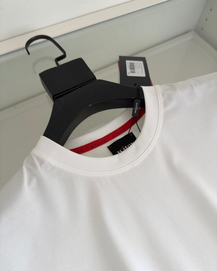 Maglietta bianca minimalista con dettaglio rosso sul colletto e tag, stile casual e versatile.