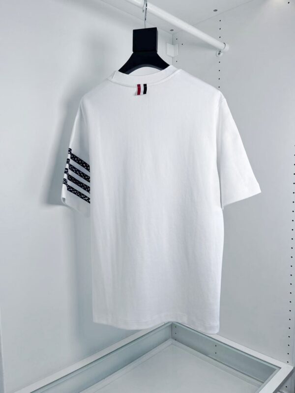 T-shirt bianco casual con strisce nere e dettaglio rosso, stile sportivo e versatile.