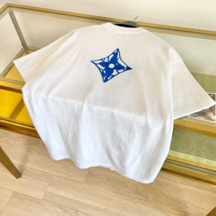 Maglietta bianca con grafica blu a stella su tavolo di vetro, stile minimalista e moderno.