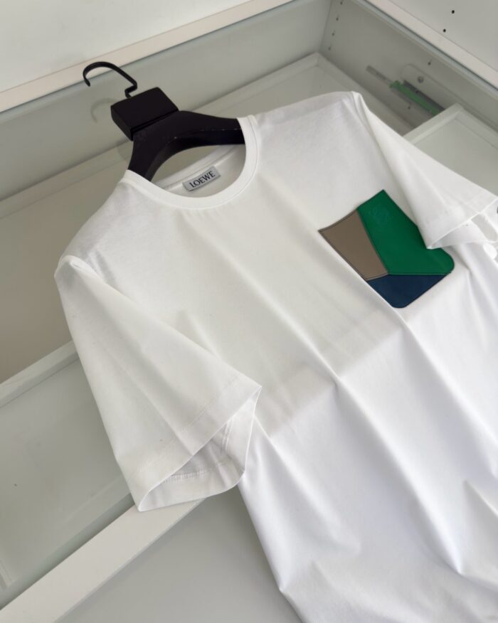T-shirt bianca con tasca geometrica colorata, eleganza casual e dettaglio artistico distintivo.