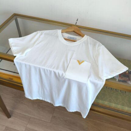 Maglietta bianca minimalista con tasca gialla su tavolo di vetro naturale, stile elegante e casual.