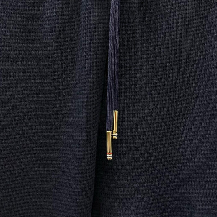 Dettaglio di tessuto nero, drizzina con aglet dorato, stile minimalista e confortevole.