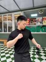 Giovane alla moda davanti a locale retro, con occhiali e polo nera, atmosfera vivace.