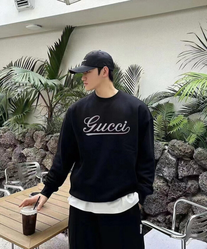 Giovane uomo casual con sweatshirt Gucci, cappello, in ambiente urbano con piante verdi.
