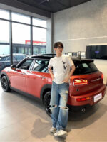 Giovane uomo con auto arancione nel showroom moderno, stile casual e atmosfera di lusso.