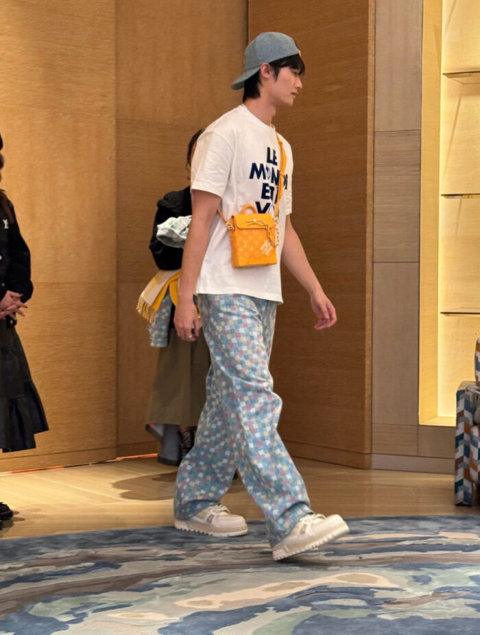 Giovane in streetwear con cappello blu e borsa arancione in ambiente moderno ed elegante.